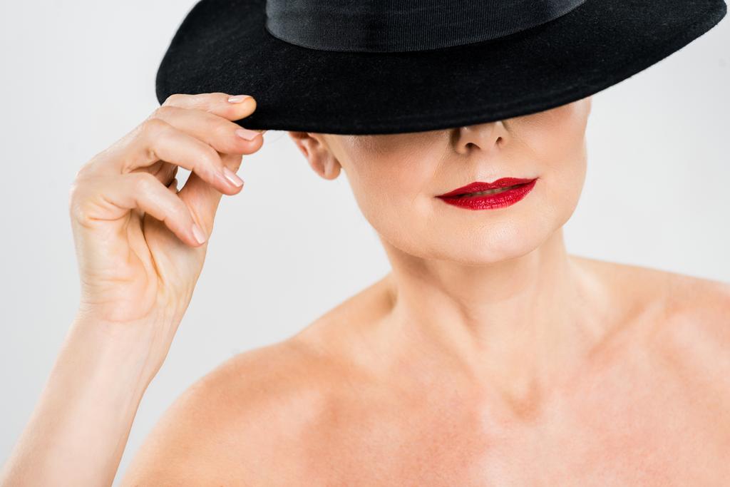 mujer de mediana edad elegante y de moda con labios rojos tocando sombrero negro aislado en gris
  - Foto, Imagen