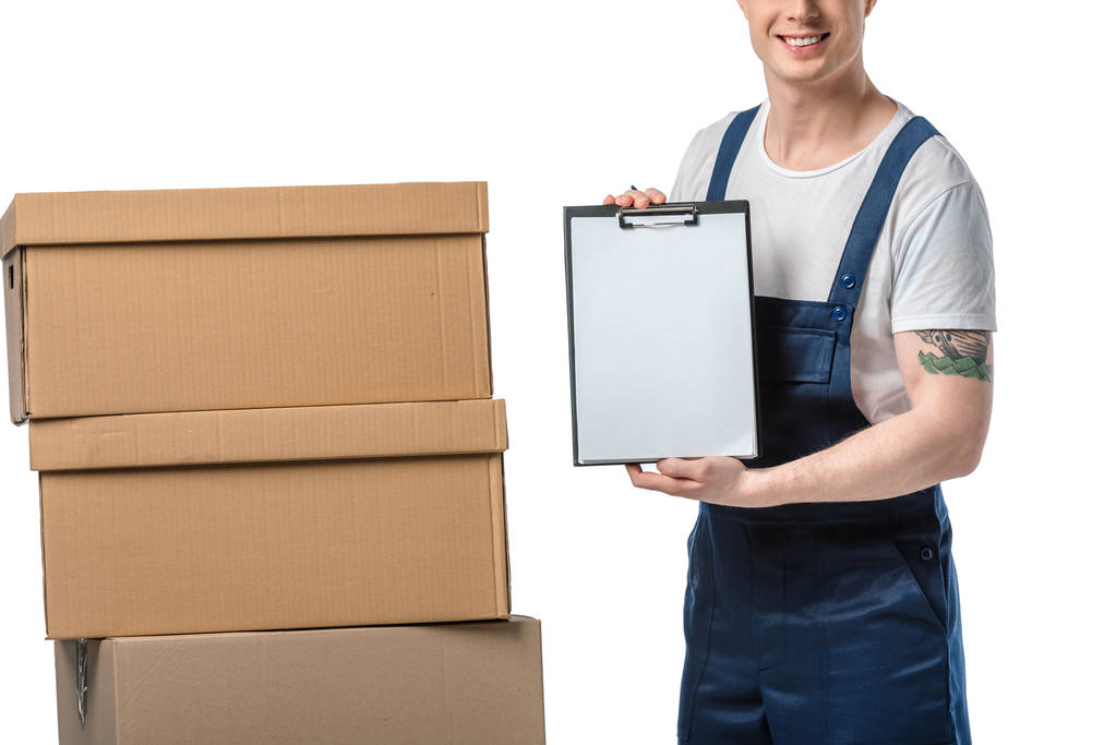 vue recadrée du déménageur en uniforme tenant le presse-papiers vierges près des boîtes en carton isolées sur blanc
 - Photo, image