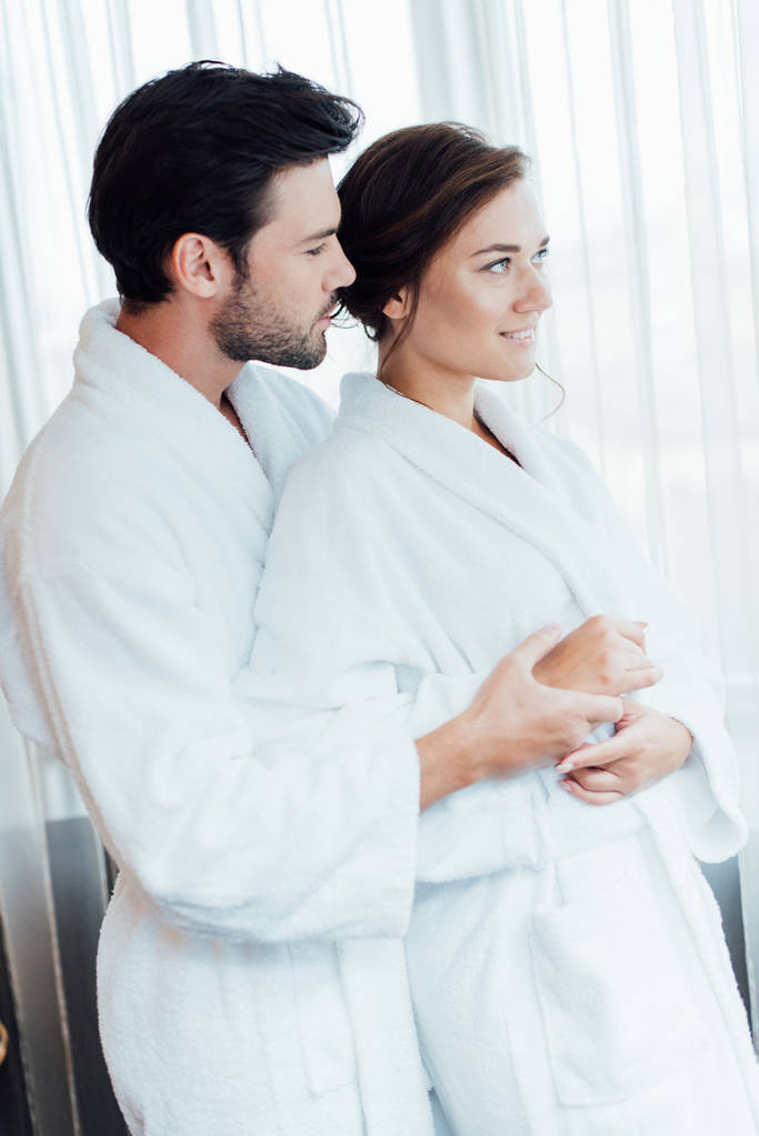 glückliches Paar in weißen Bademänteln umarmt sich im Hotel  - Foto, Bild