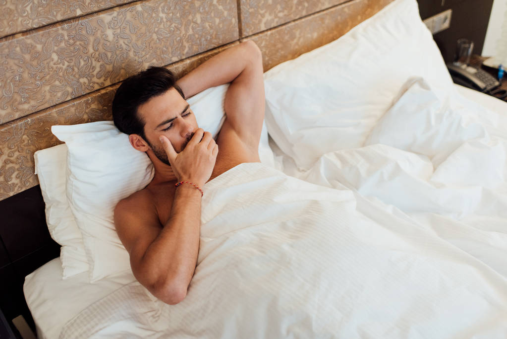 vista aerea di bell'uomo che copre la bocca mentre sbadiglia a letto
 - Foto, immagini