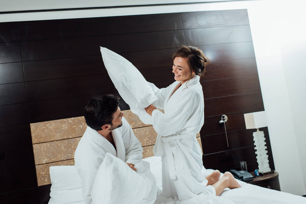 ευτυχισμένο ζευγάρι έχοντας μαξιλάρι καταπολέμηση σε κρεβάτι στο ξενοδοχείο  - Φωτογραφία, εικόνα