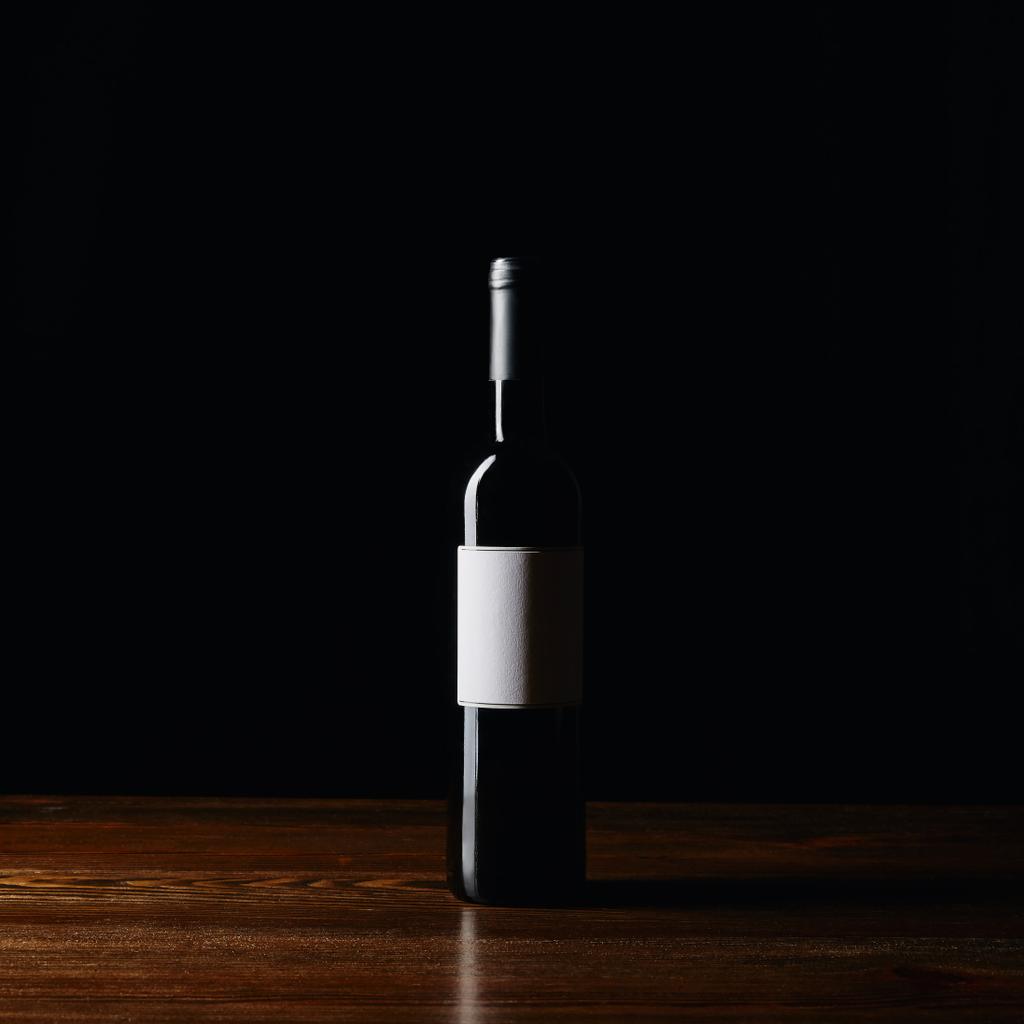 黒に分離された木製の表面に空白のラベルのワイン瓶 - 写真・画像