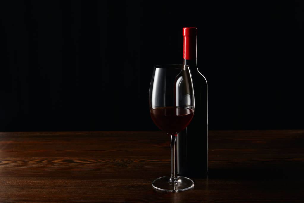 ボトルと黒に分離された木製の表面に赤ワインのガラス - 写真・画像