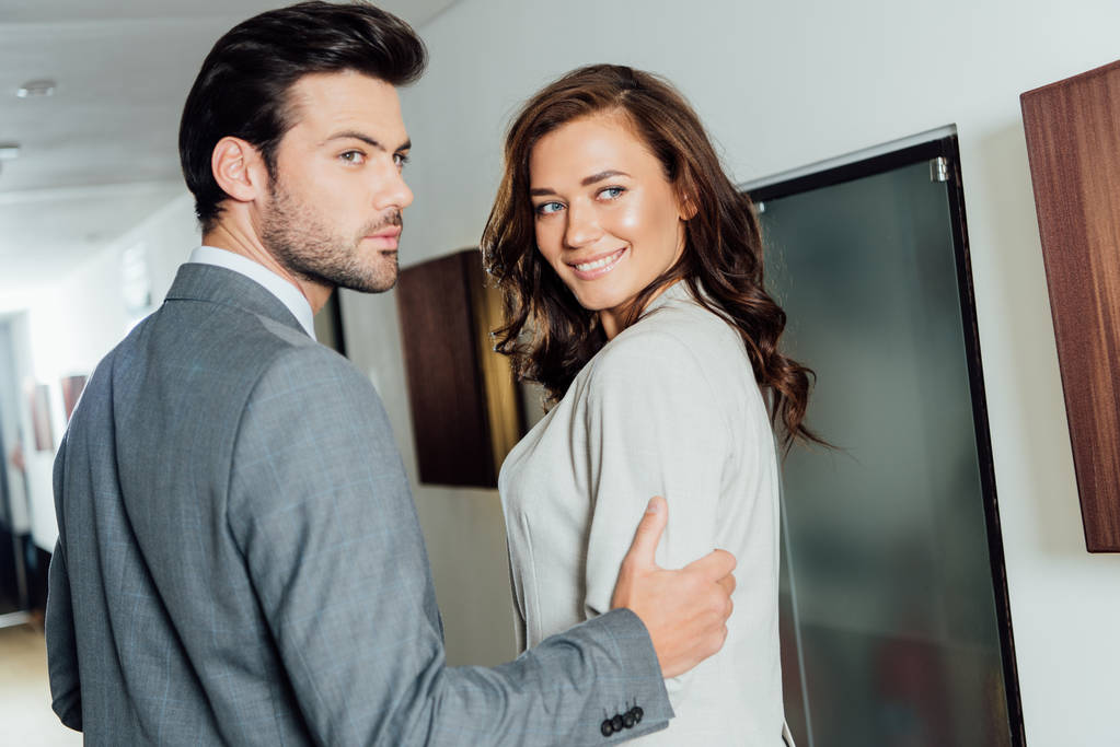 впевнений бізнесмен торкається руки весела бізнес-леді в формальному носінні, стоячи в готельному коридорі
  - Фото, зображення