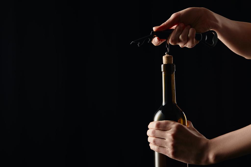 Teilansicht der Frau beim Öffnen einer Weinflasche mit Korkenzieher isoliert auf schwarz - Foto, Bild