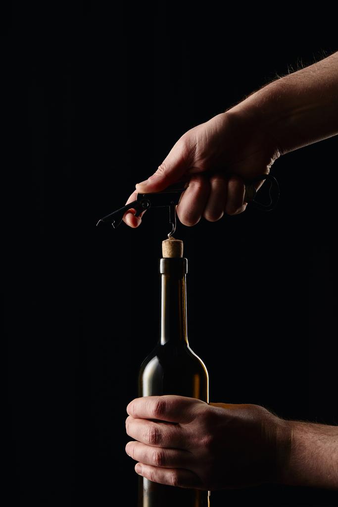 Vista parcial del hombre abriendo botella de vino con sacacorchos aislados en negro
 - Foto, imagen