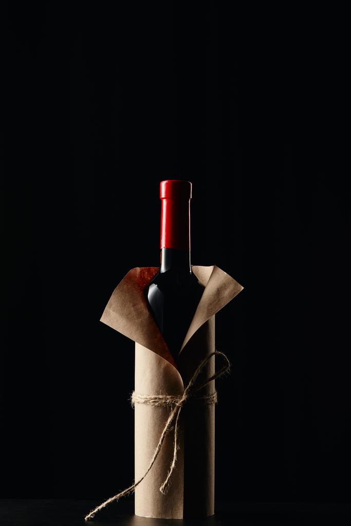 Botella de vino envuelta en papel sobre superficie oscura aislada sobre negro
 - Foto, imagen