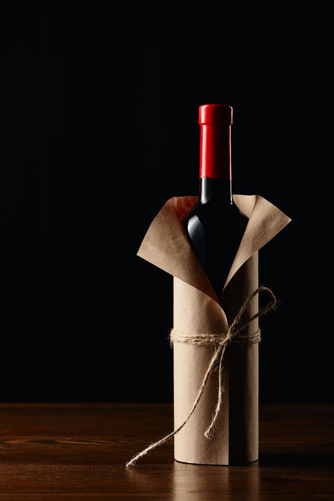 Garrafa de vinho em papel de embrulho na superfície de madeira isolada em preto
 - Foto, Imagem