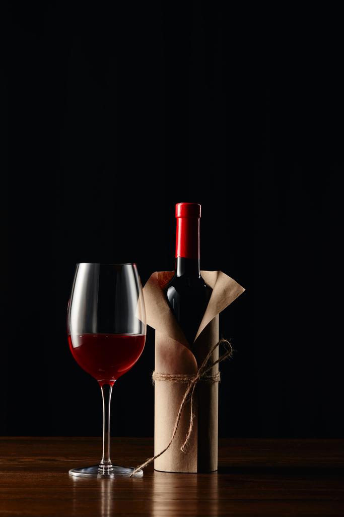 Kieliszek do wina i butelki w opakowaniu papieru na powierzchni drewnianych na czarnym tle - Zdjęcie, obraz