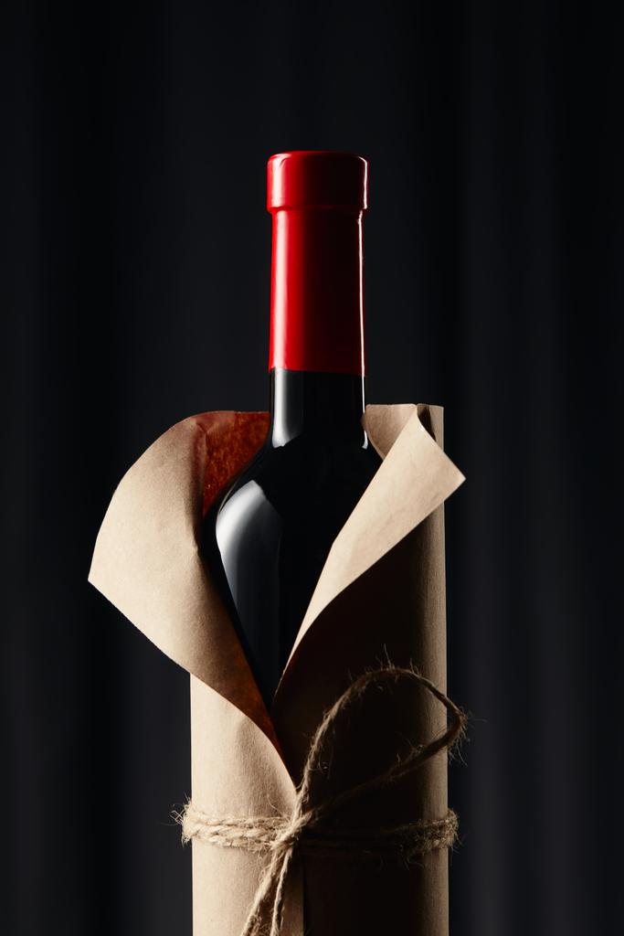 Glas wijn fles in papier wrapper op donker - Foto, afbeelding
