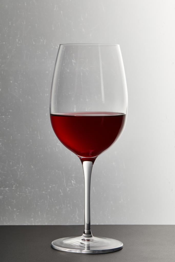Wine glass with burgundy red wine on dark surface on grey - Photo, Image