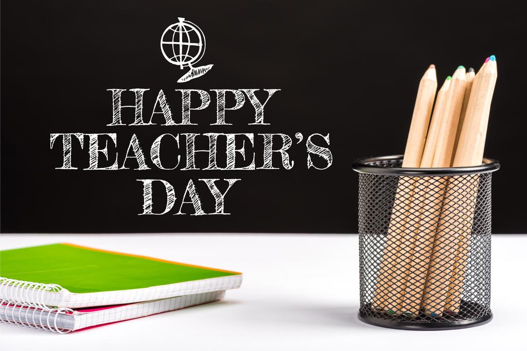 notebooky a barevné tužky na stůl s bílým šťastný učitelé den nápis na černém pozadí  - Fotografie, Obrázek