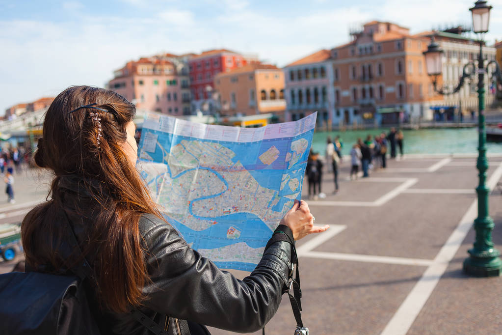 junge Frau schaut an sonnigem Tag auf Papierkarte von Venedig, viele Touristen im Hintergrund - Foto, Bild