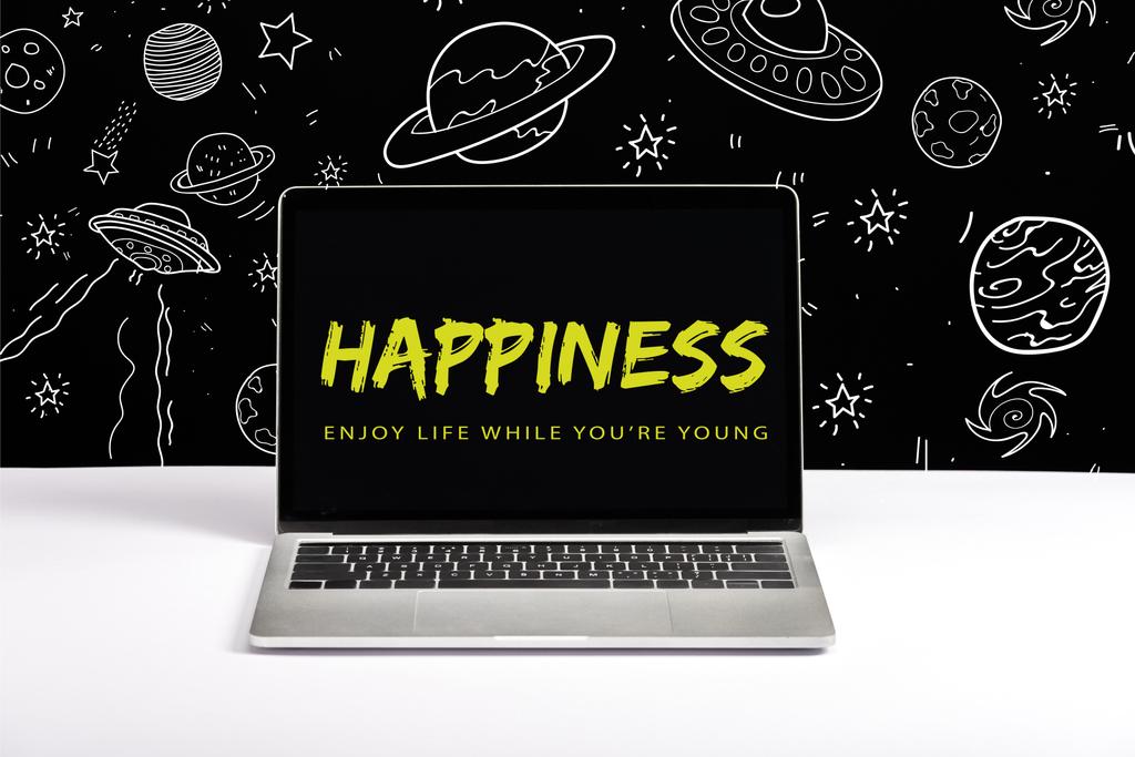 ноутбук на столі з насолодою життям, поки ти молодий і щасливий, пропускаючи на екрані з ілюстрацією білої галактики на чорному
  - Фото, зображення