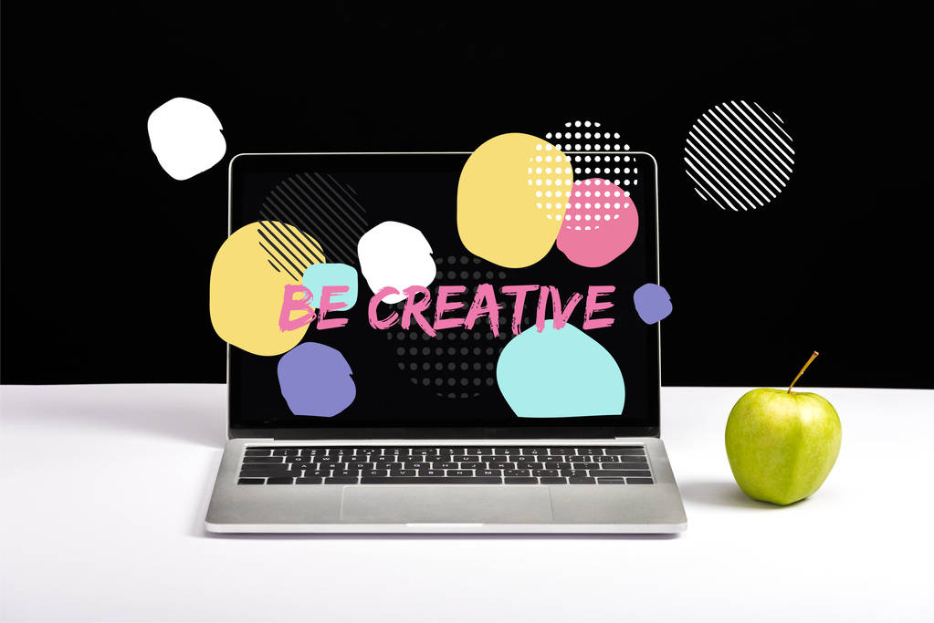 frischer grüner Apfel und Laptop auf dem Tisch mit kreativen Schriftzügen auf dem Bildschirm und abstrakten Kreisen auf schwarzem Hintergrund - Foto, Bild