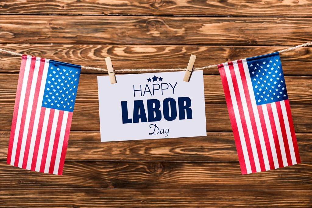 card with happy labor day lettering hanging on string with pins and american flags on wooden background - Photo, Image