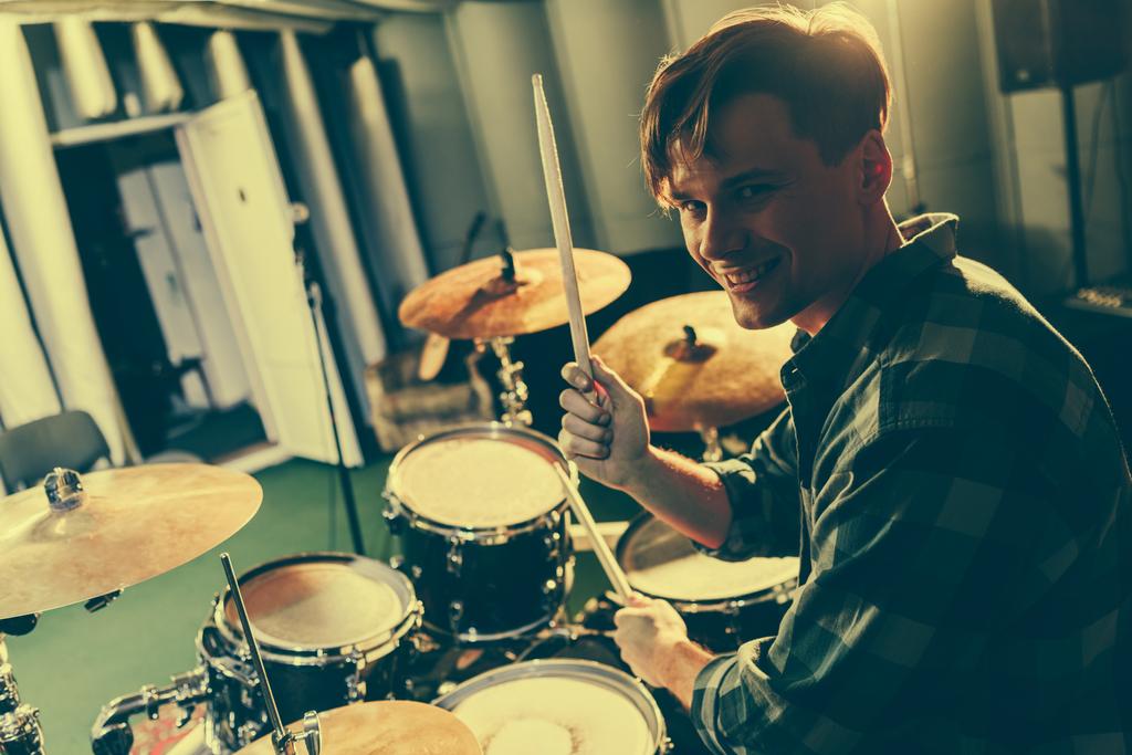 счастливый симпатичный музыкант держит барабаны палочками возле барабанов
 - Фото, изображение