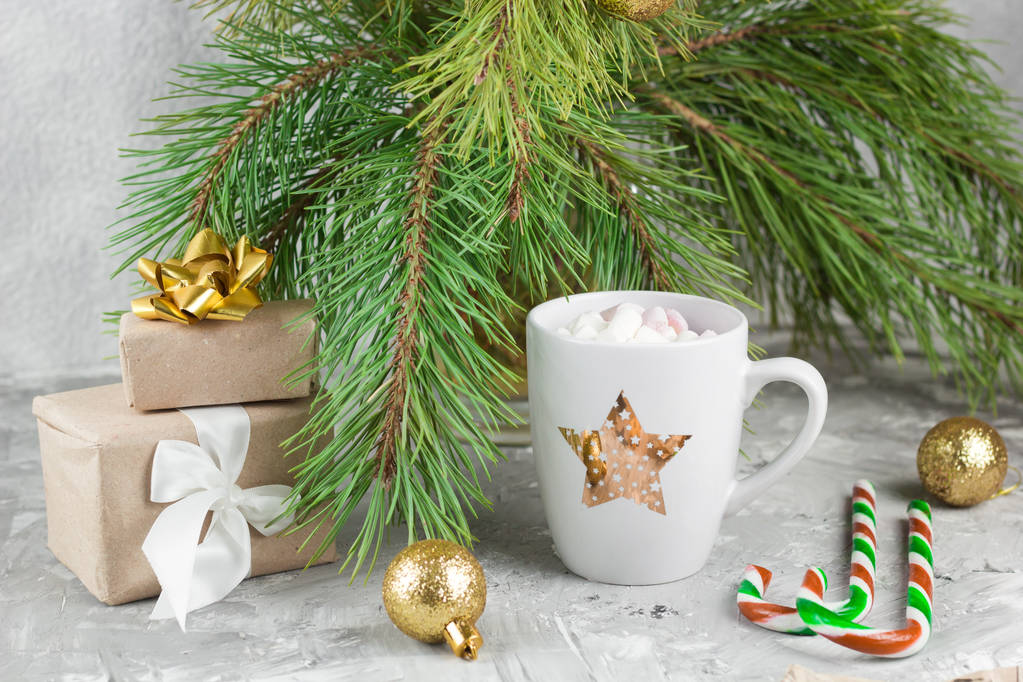 gift boxes, hot drink with marshmallows, candy canes and golden balls on shabby gray background with evergreen christmas tree branches - Photo, Image