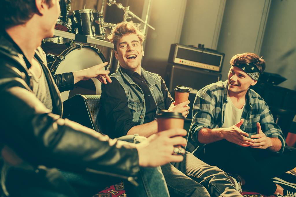 selective focus of happy rock band laughing while talking and holding paper cups  - Photo, Image