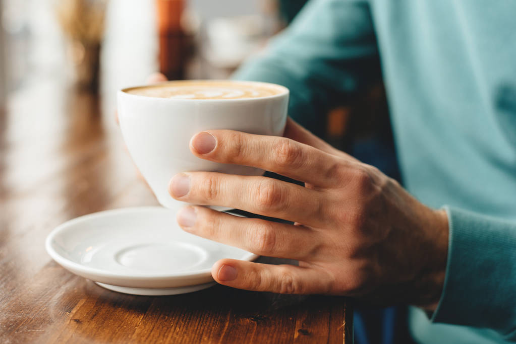A xícara de cappuccino nas mãos
 - Foto, Imagem
