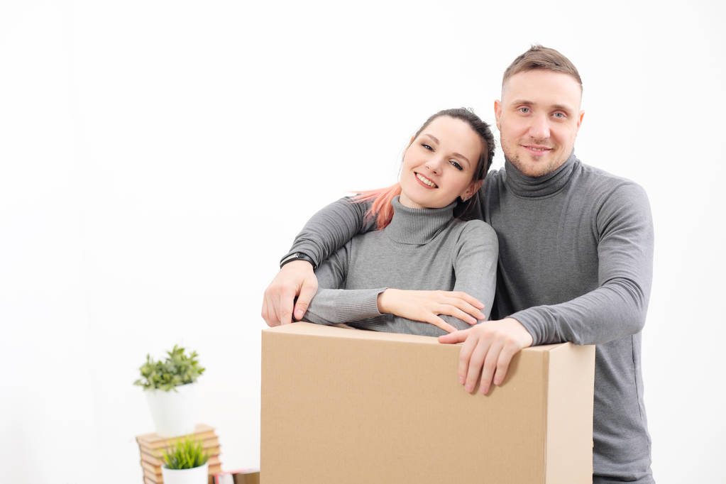 Eine junge Familie, ein Mann und eine Frau in grauen Pullovern ziehen in eine neue Wohnung. Kisten mit Fracht auf weißem Hintergrund. - Foto, Bild