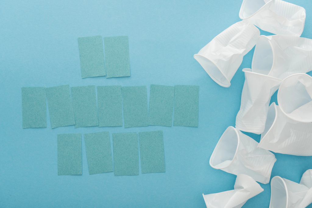pohled shora bílých plastových kelímků a prázdné poznámek sticky notes s prostorem kopie na modrém pozadí  - Fotografie, Obrázek