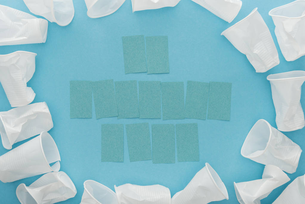 Draufsicht auf weiße Plastikbecher und leere Haftnotizen mit Kopierraum auf blauem Hintergrund  - Foto, Bild