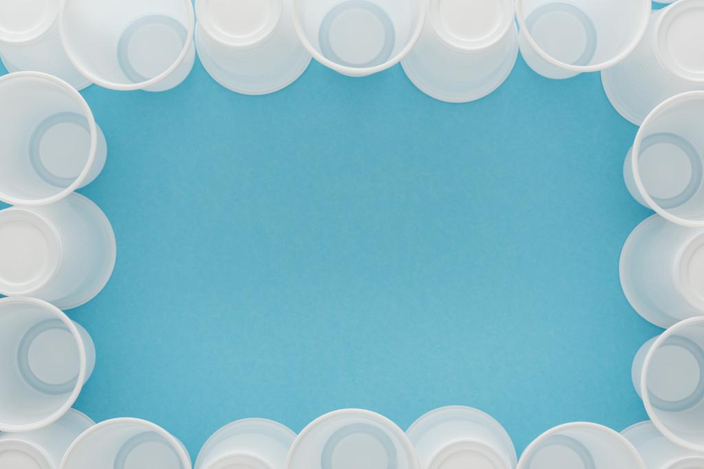 bovenaanzicht van witte plastic bekers op blauwe achtergrond met kopie ruimte  - Foto, afbeelding