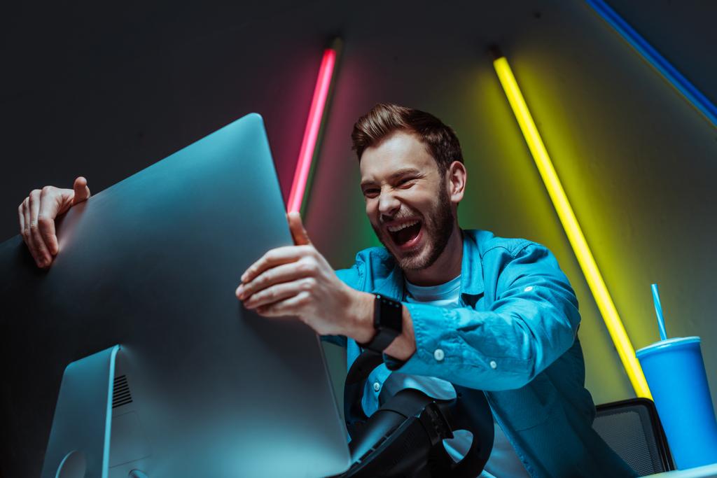 hombre guapo y feliz sonriendo y sosteniendo monitor de computadora
  - Foto, Imagen
