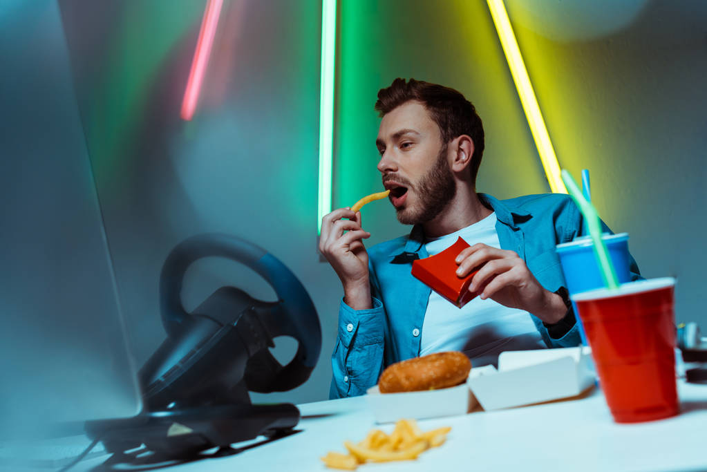 hyvännäköinen ja komea mies syö ranskalaisia perunoita ja katselee tietokonenäyttöä
  - Valokuva, kuva