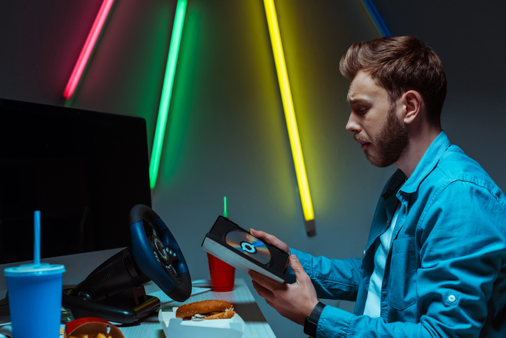 vista lateral del hombre guapo y guapo sosteniendo un disco compacto con videojuego
  - Foto, Imagen