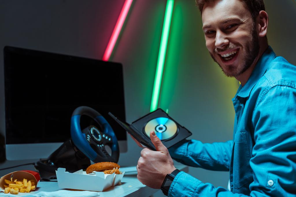 όμορφος και χαμογελαστός άνθρωπος κρατώντας συμπαγή δίσκο με βιντεοπαιχνίδι και δείχνοντας σαν - Φωτογραφία, εικόνα