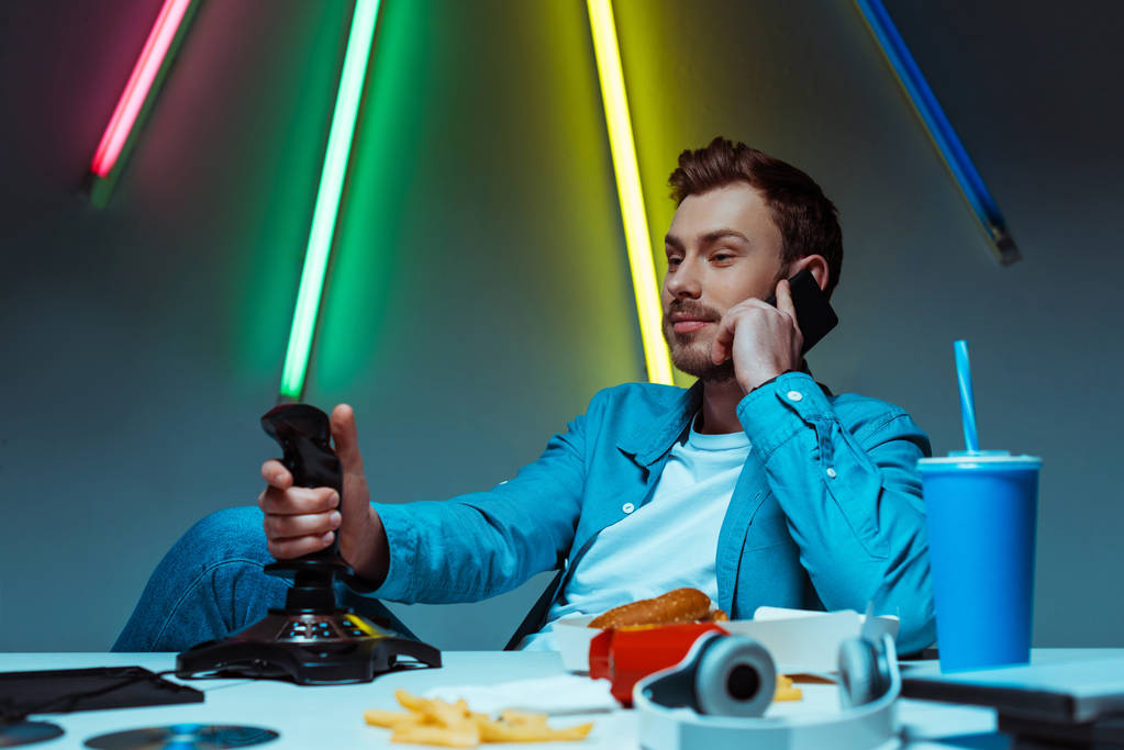 selective focus of handsome man talking on smartphone and holding joystick - Photo, Image