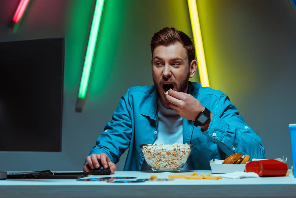 pohledný a hezký muž držící počítačovou myš a jíst popcorn  - Fotografie, Obrázek