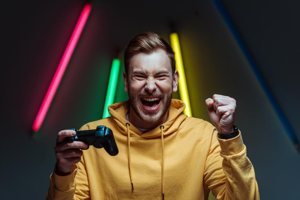 young adult handsome and screaming man looking at camera and holding gamepad - Photo, Image