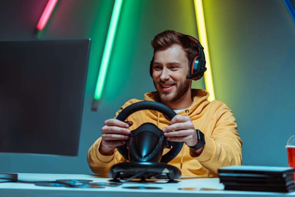 young adult and handsome man in headphones playing video game with steering wheel - Photo, Image