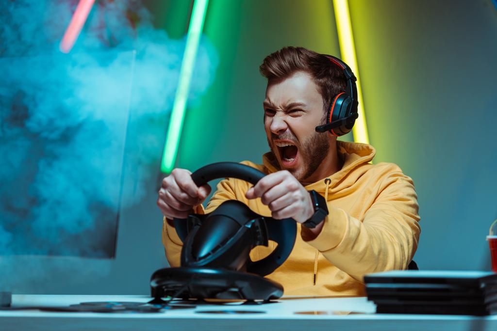 сердитий і красивий чоловік в навушниках грає в відеогру з кермом
 - Фото, зображення