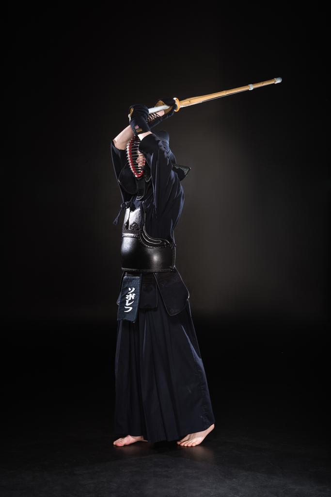 Vista a tutta lunghezza del combattente kendo che pratica con la spada di bambù sul nero
 - Foto, immagini