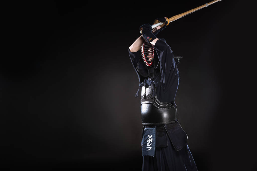 Kendo-Kämpfer in traditionellem Helm übt mit Bambusschwert auf schwarz - Foto, Bild