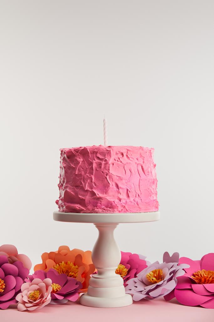 ケーキの上の蝋燭とピンクの誕生日ケーキが灰色の紙の花の近くに立つ - 写真・画像