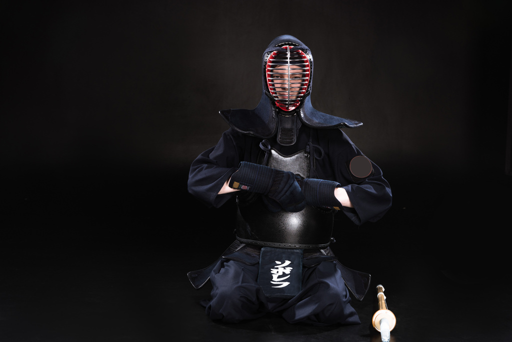 Kendo fighter in helmet sitting on floor and taking off gloves on black - Photo, Image