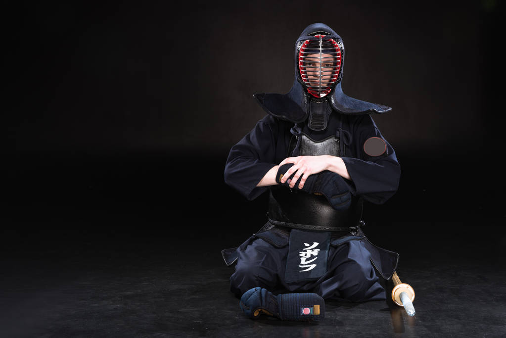 Kendo-Kämpfer mit Helm sitzt auf dem Boden und zieht Handschuh auf schwarz aus - Foto, Bild
