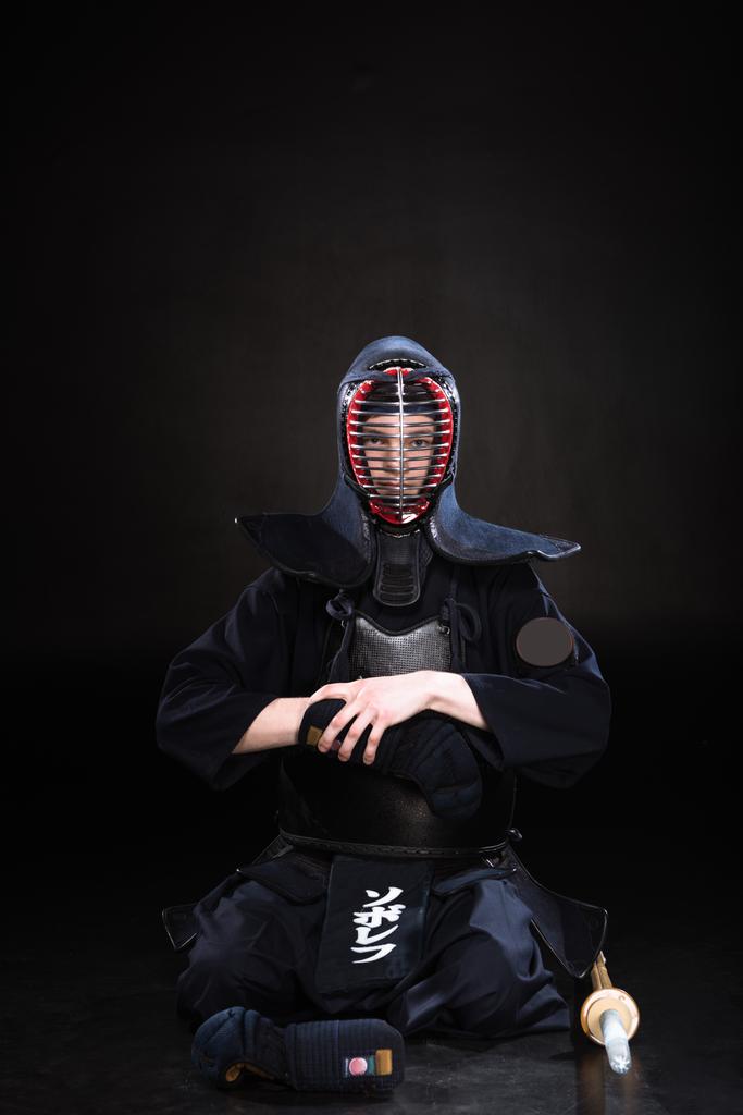 Kendo luchador en casco sentado en el suelo y quitándose el guante en negro
 - Foto, imagen