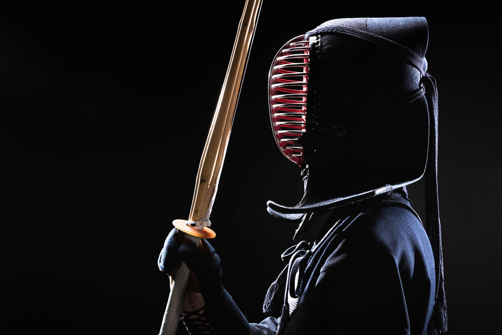 Vue latérale du combattant kendo en casque traditionnel tenant épée de bambou sur noir
 - Photo, image