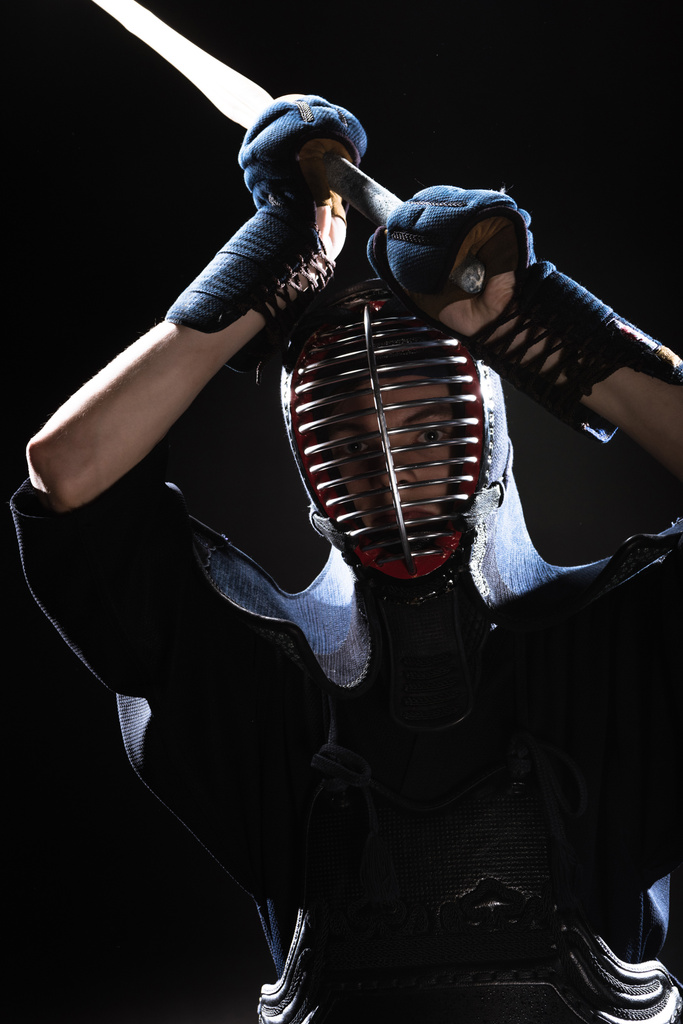 Combatiente Kendo en armadura practicando con espada de bambú y mirando a la cámara en negro
 - Foto, imagen