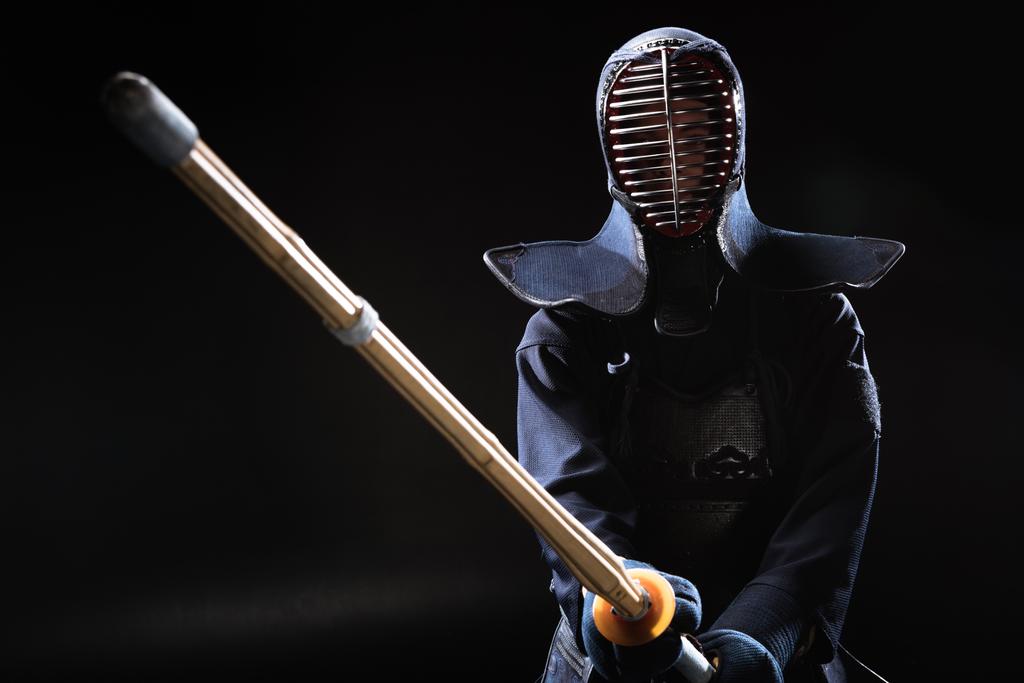 Kendo fighter in helmet holding bamboo sword on black - Photo, Image