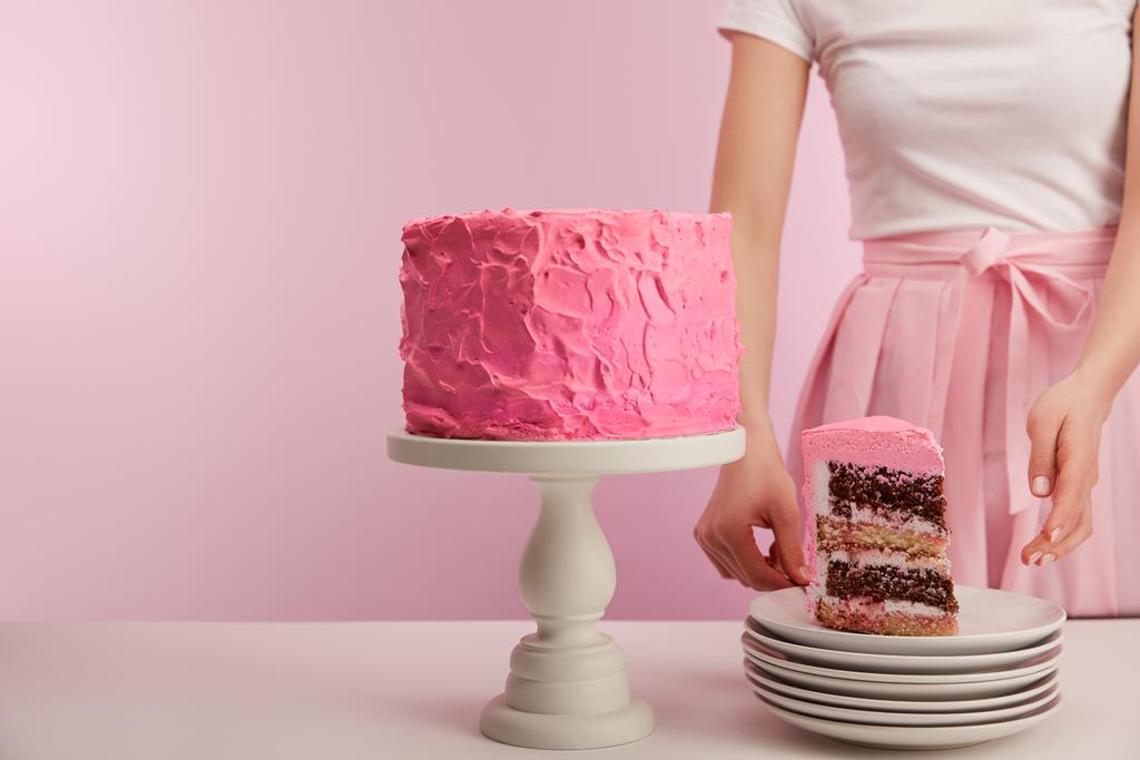 abgeschnittene Ansicht einer Frau, die neben einem Stück süßer Geburtstagstorte in weißer Untertasse auf rosa steht - Foto, Bild