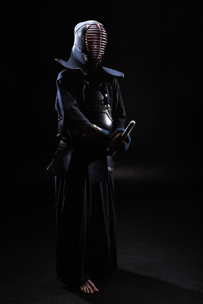 Vista completa de kendo fighter en casco sosteniendo espada de bambú sobre negro
 - Foto, imagen