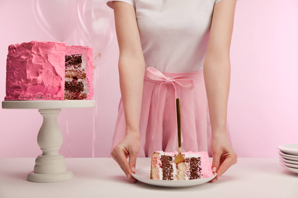 bijgesneden beeld van vrouw met plaat met stuk heerlijke verjaardagscake en gouden vork op roze - Foto, afbeelding