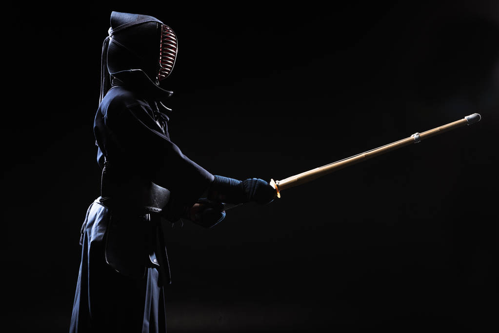 Kendo fighter in helmet holding bamboo sword on black - Photo, Image